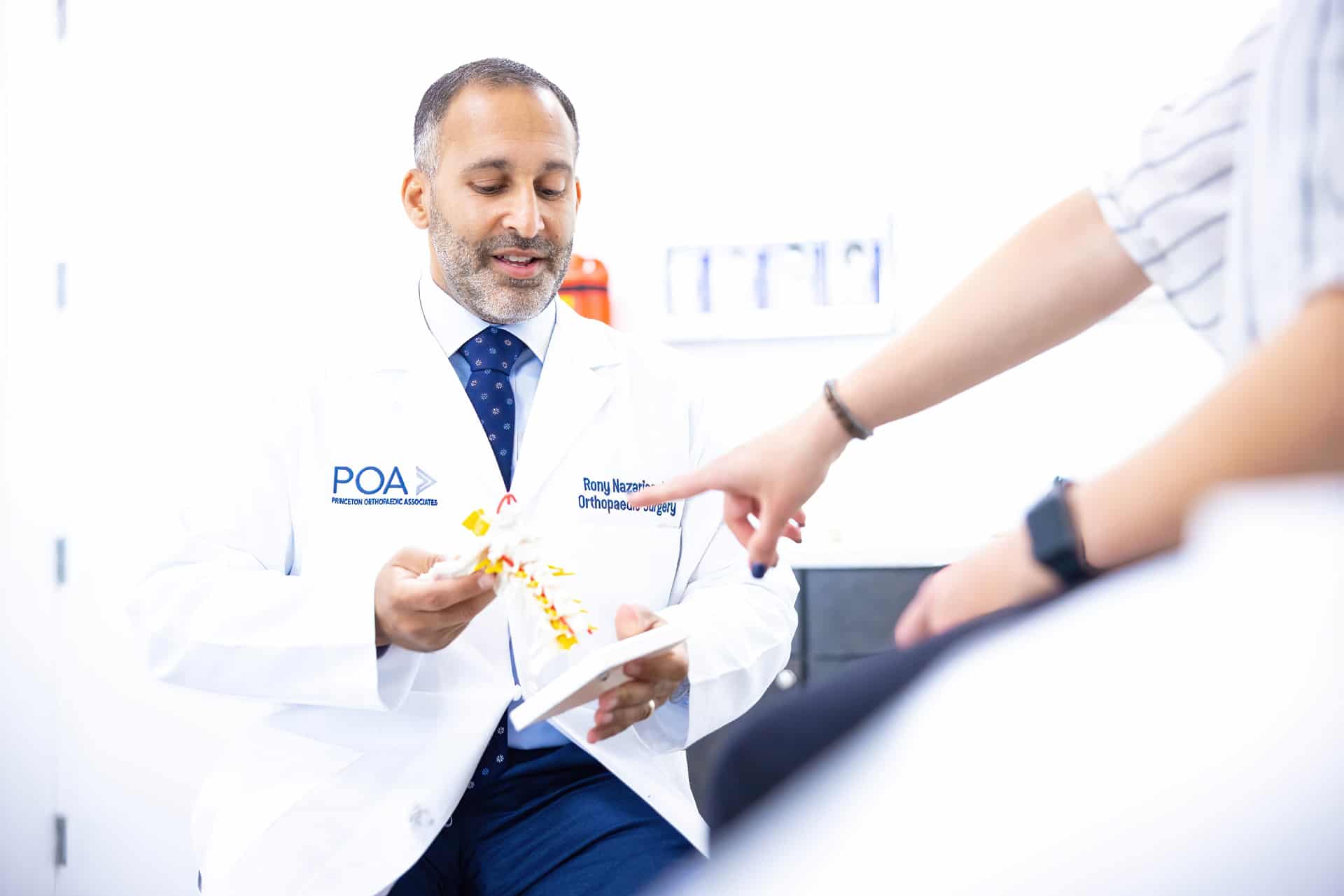 Dr. Nazarian from princeton orthopedic associates shows a patient a model of a spine as he explains back pain and lower back stretches.