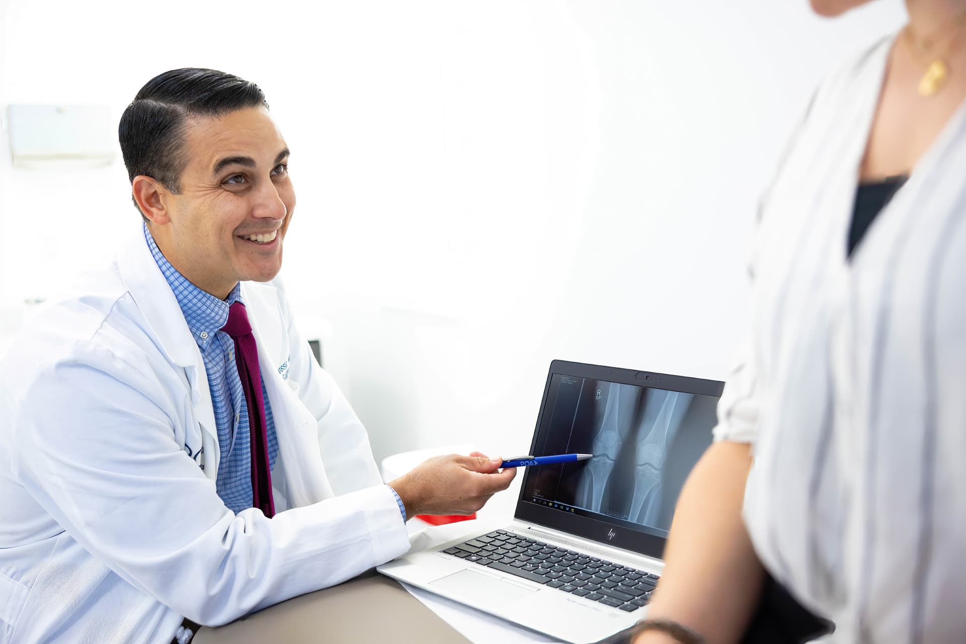 Dr. Rossy explaining hoffa fat pad to a patient while he points to the xray on the laptop screen.