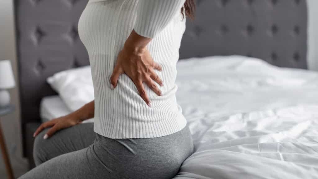 Woman with back pain sitting on her bed at home