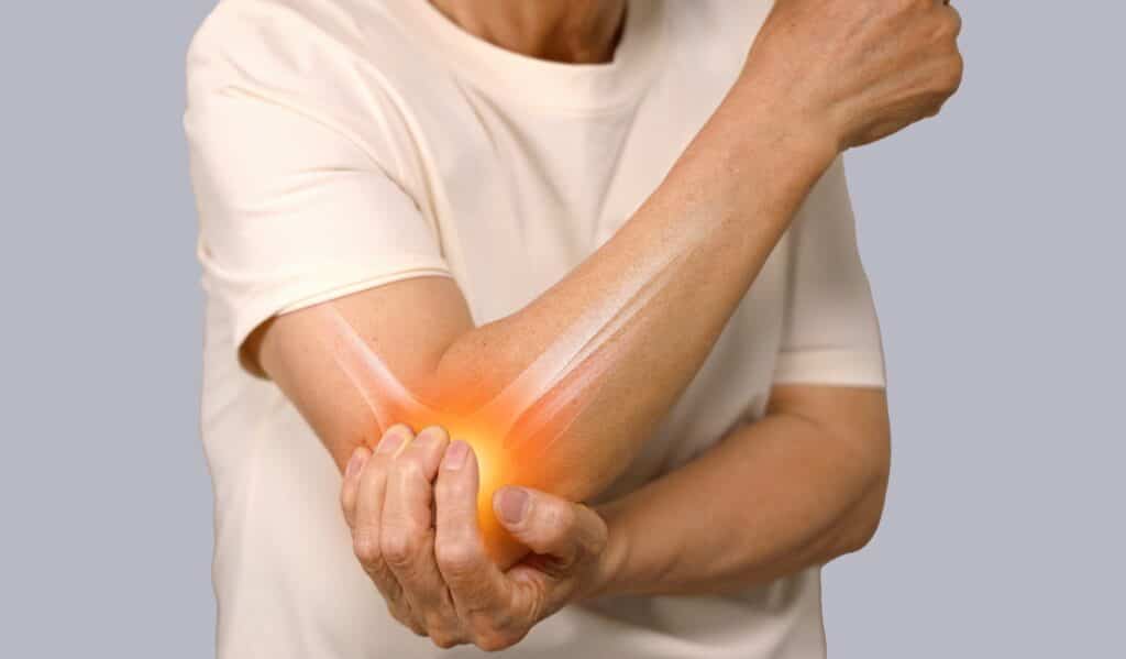 Close up of woman holding elbow from pain caused by elbow tendinopathy. 