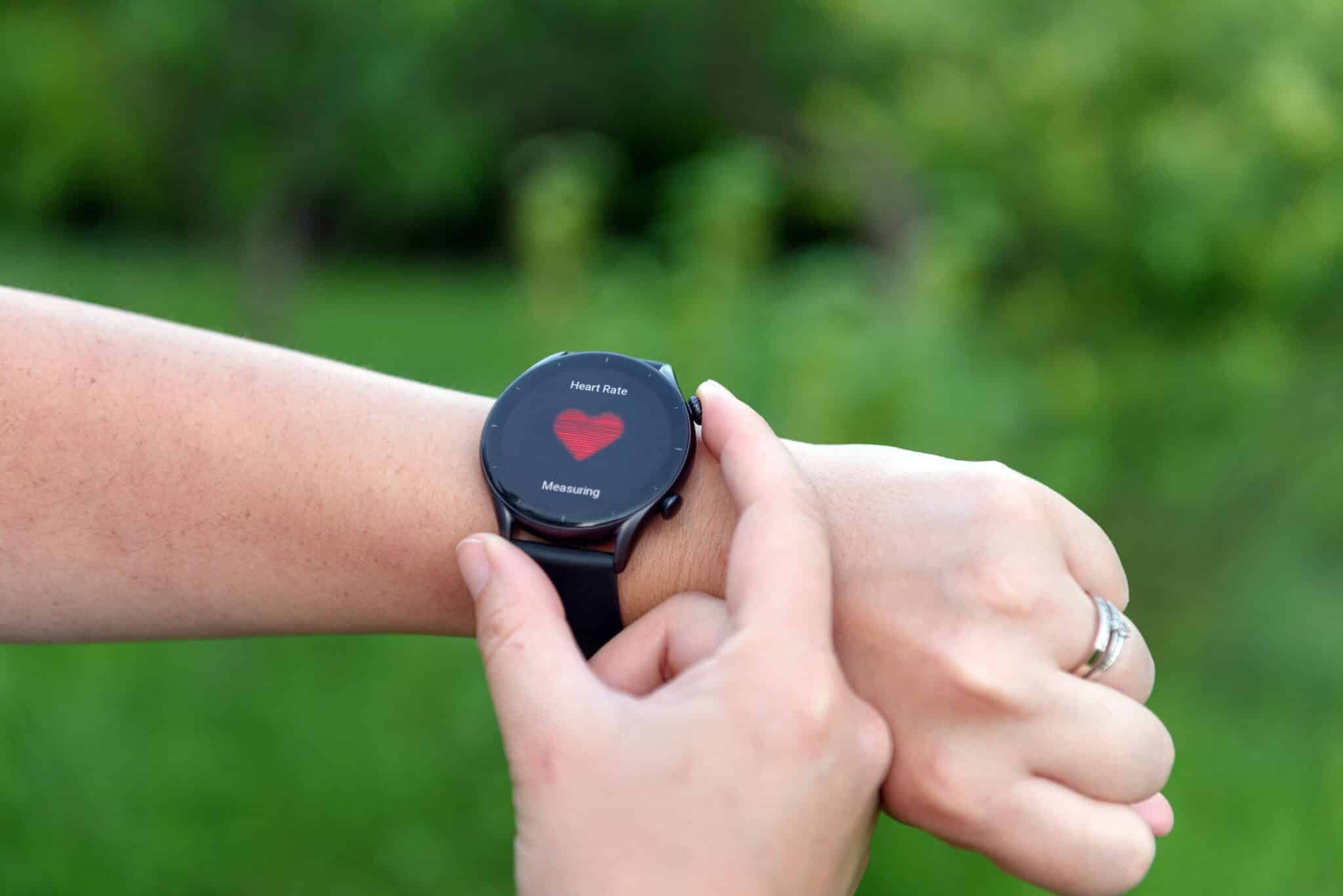 Smartwatch on a wrist displaying a heart-rate reading outdoors.