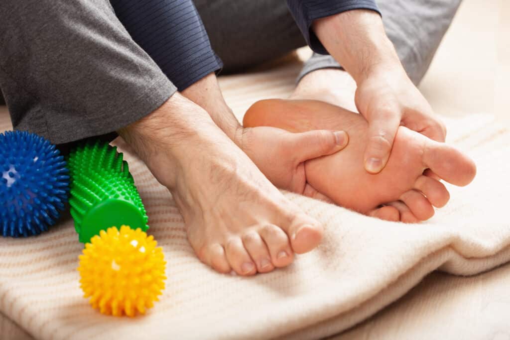 man doing flatfoot correction self massage at home - Princeton Orthopaedic Associates Close-up of an adult hand massaging a baby’s feet on a soft blanket, with colorful spiky massage balls nearby.