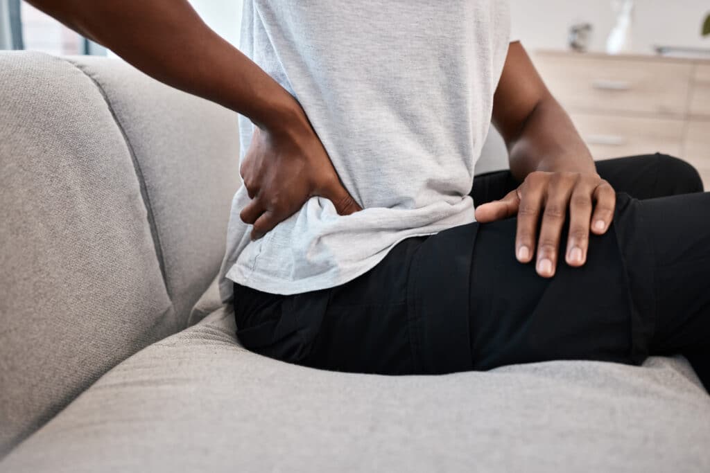 Adult massaging the lower back while sitting on a couch at home