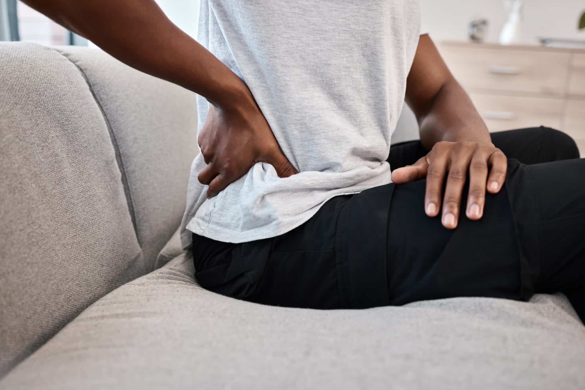 adult-massaging-lower-back-while-sitting-on-couch-2026-03-25-08-09-57-utc - Princeton Orthopaedic Associates poa hip issues explained