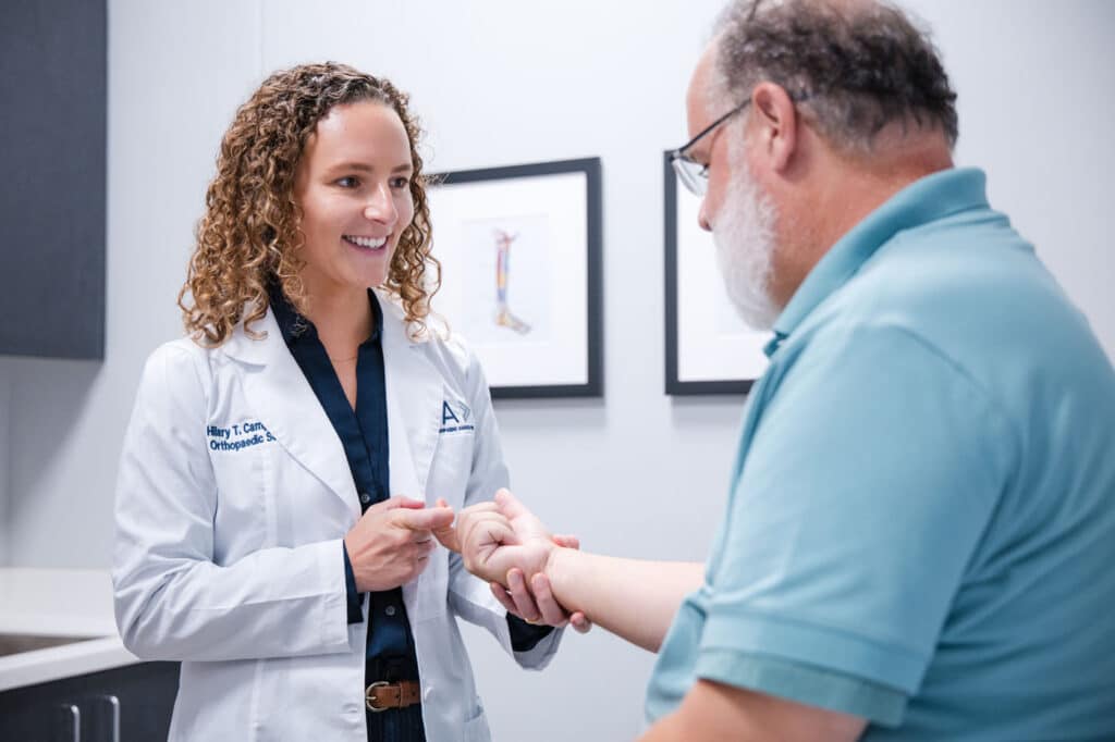 Princeton Orthopaedic Associates - 2026 - Dr Campell-2 - Princeton Orthopaedic Associates Female orthopedic doctor in a white coat smiles while gently holding a patient's hand during a consultation.