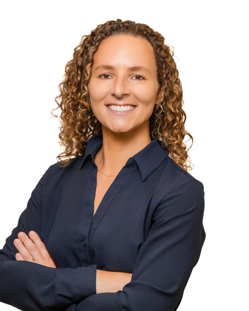 pp_Princeton Orthopaedic Associates - 2026 - -13_04 Waist Up 8x10 - Princeton Orthopaedic Associates Smiling woman with curly brown hair wearing a navy shirt, arms crossed against a white background.