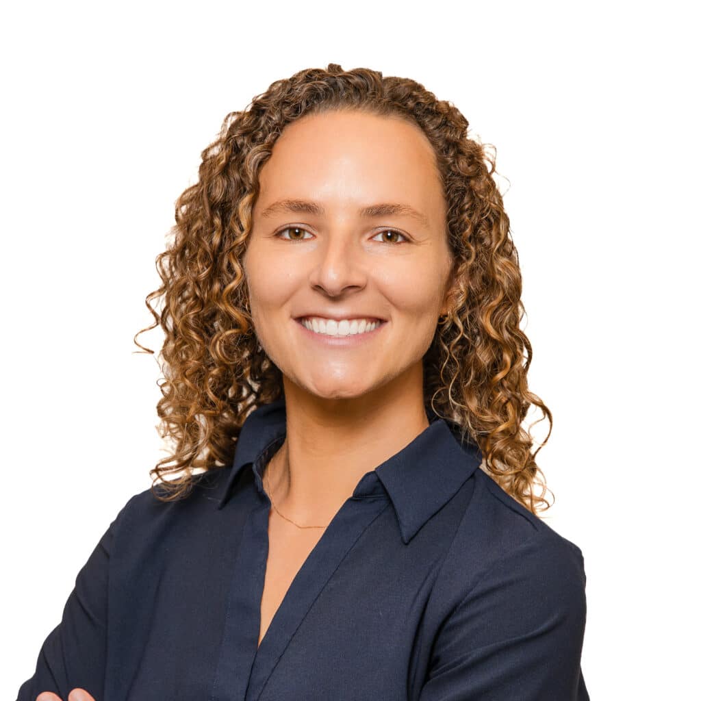 Close-up of a smiling woman with curly brown hair wearing a navy shirt, cropped at shoulders.