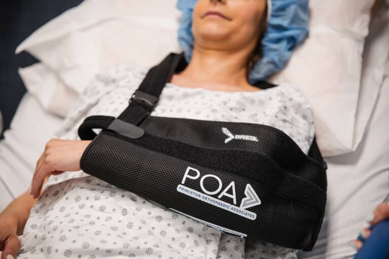 Patient lying in a hospital bed wearing a black orthopedic chest brace over a patterned gown.