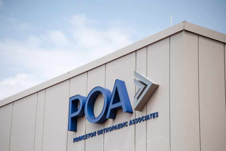 Partial view of a beige building exterior with large blue 3D letters of a medical sign (Princeton Orthopaedic Associates) against a blue sky.