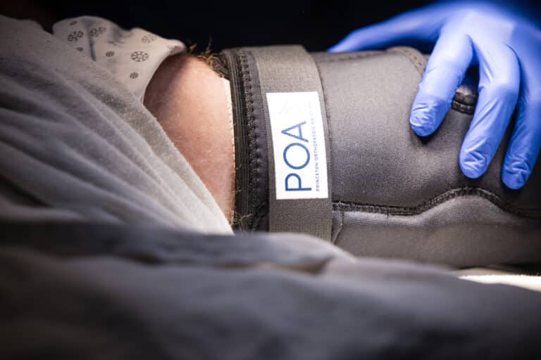 Close-up of a medical blood pressure cuff wrapped around a patient’s arm with a blue-gloved hand nearby.