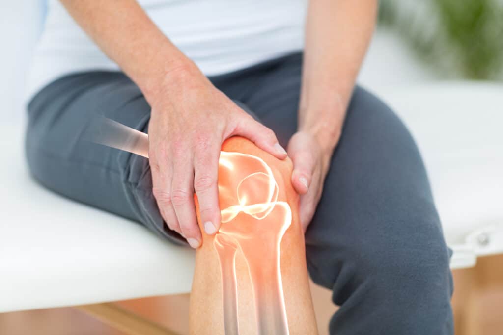 Person seated, applying pressure to a knee with a warm orange glow over the joint to indicate pain relief or injury.